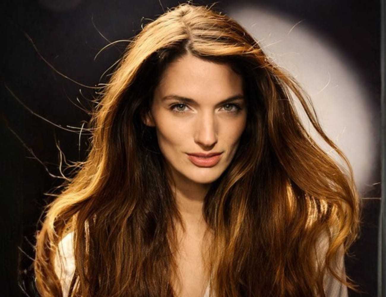 Young woman with long brown hair looks directly at the camera under soft lighting.